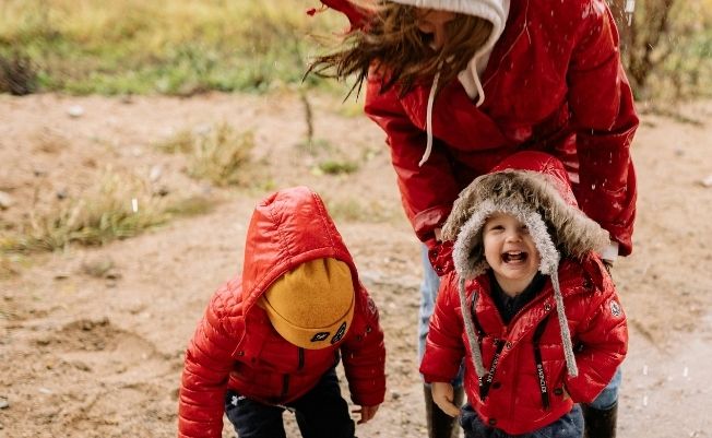 two children and a parent dressed in red coats playing outdoors in cold weather.