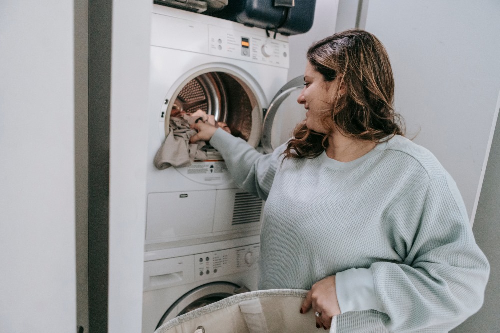 A woman is loading the washing machine in the laundry