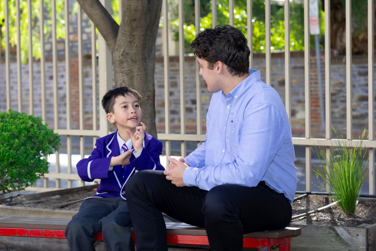 A man and a boy sit together on a bench, enjoying a moment of companionship in a park setting.
