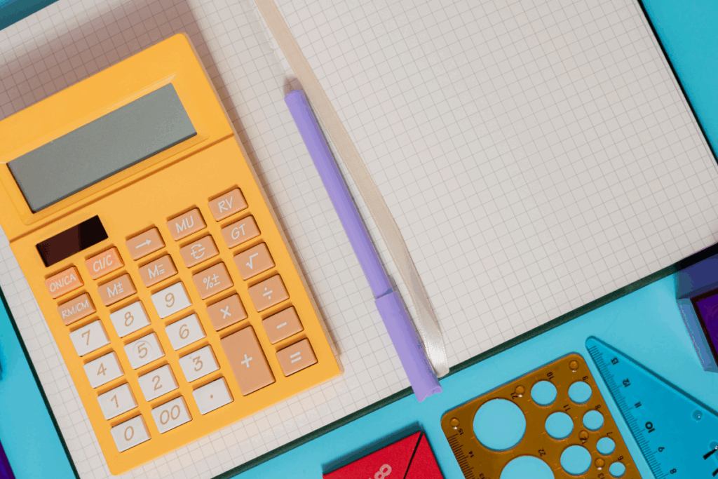 A yellow calculator, notebook, and pen arranged on a blue background.