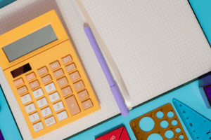 A yellow calculator, notebook, and pen arranged on a blue background.