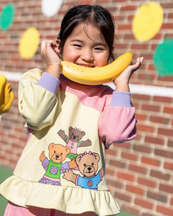 Girl smiles at camera wearing Bananas and Pyjamas long-sleeved T-shirt and holds a banana.