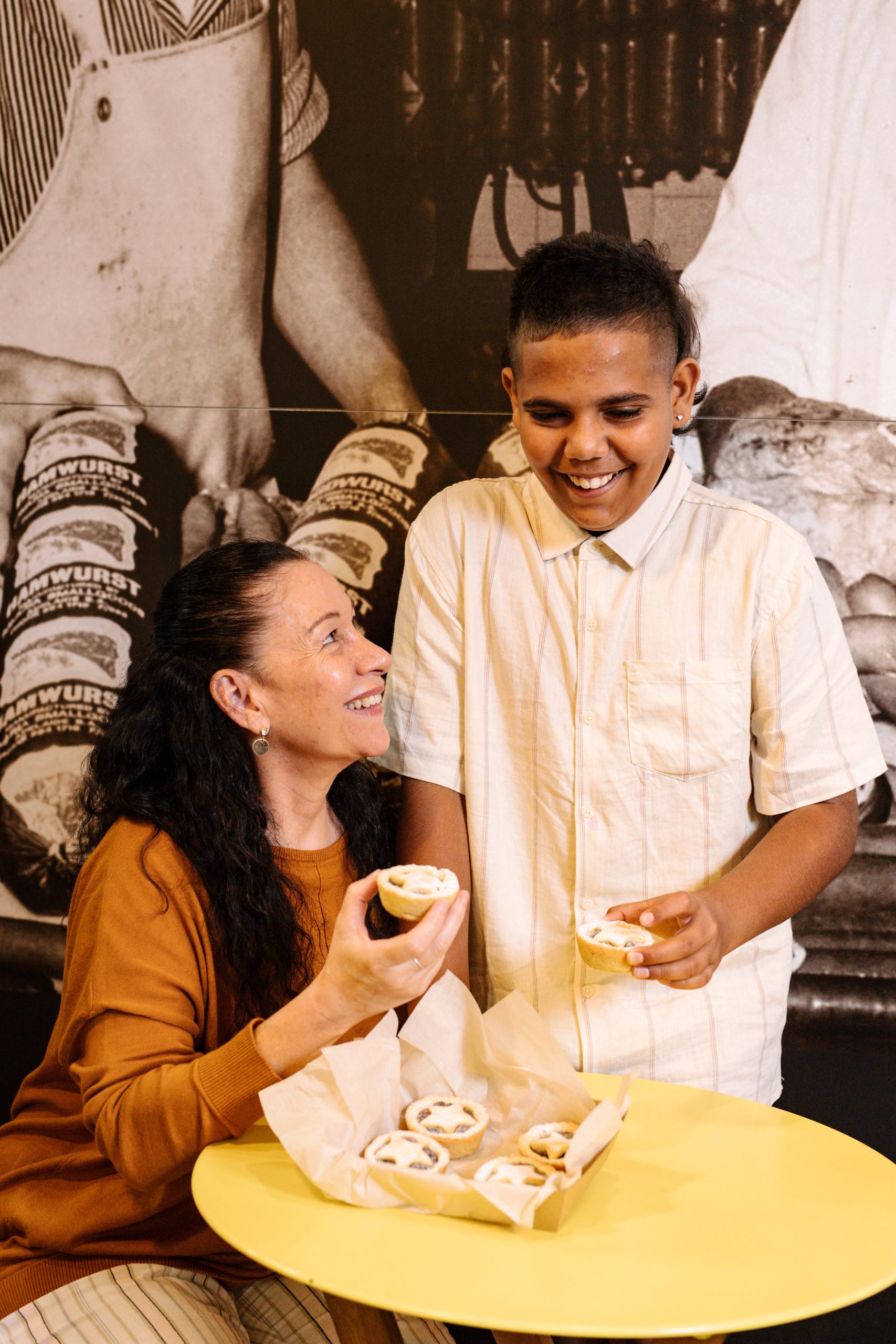 A woman and a boy enjoy doughnuts together at a table, sharing smiles and treats in a cozy setting.