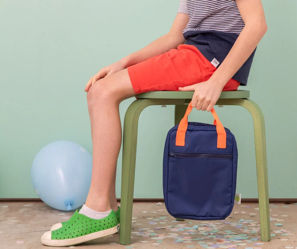 Boy holding navy and orange lunch bag.