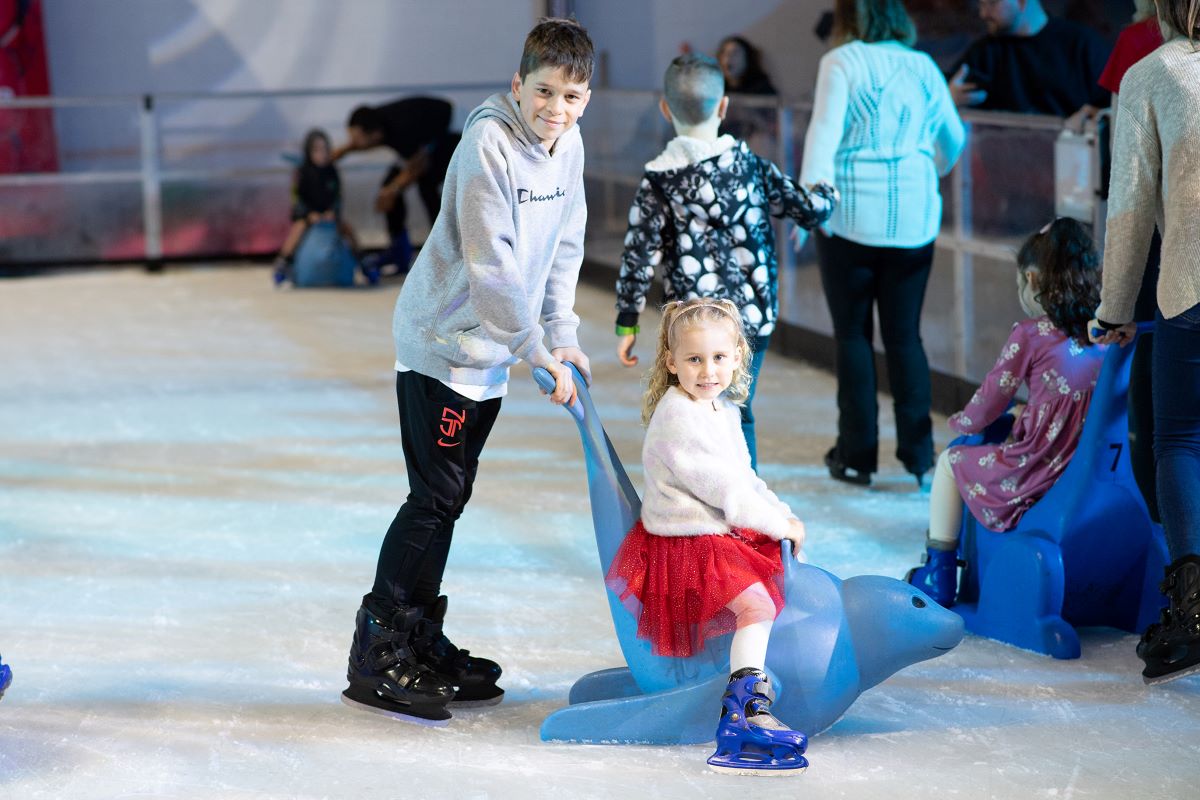 Boy pushes girl on the ice in a sled shaped as a seal.