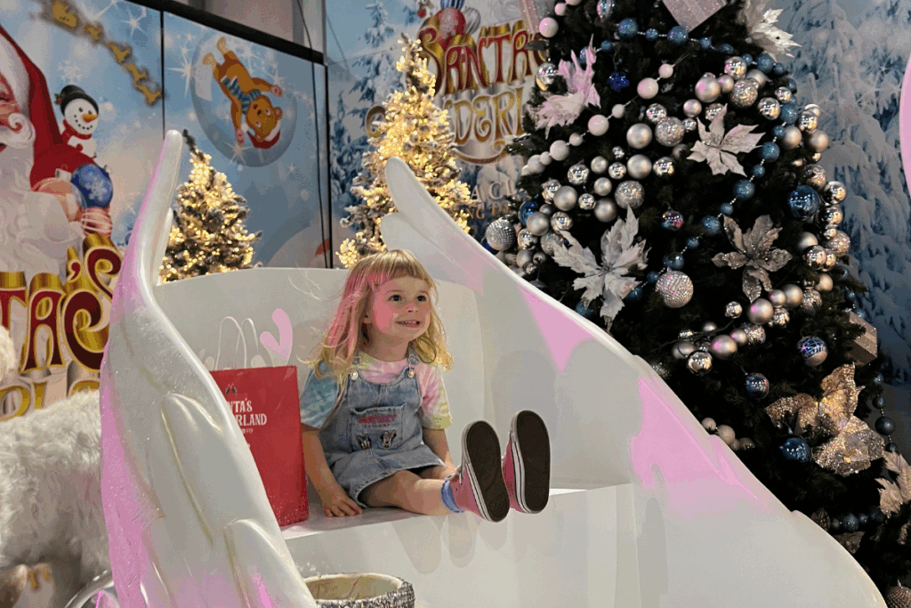 A little girl sitting in a chair next to a cheerful snowman, smiling in a winter setting.
