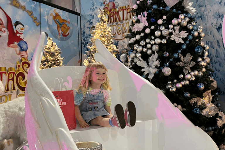 A little girl sitting in a chair next to a cheerful snowman, smiling in a winter setting.
