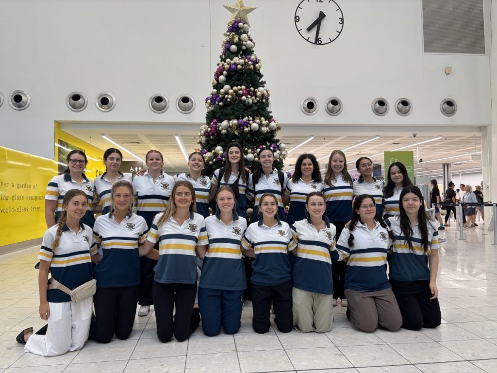 A group of women in uniform smiling together in front of a decorated Christmas tree.