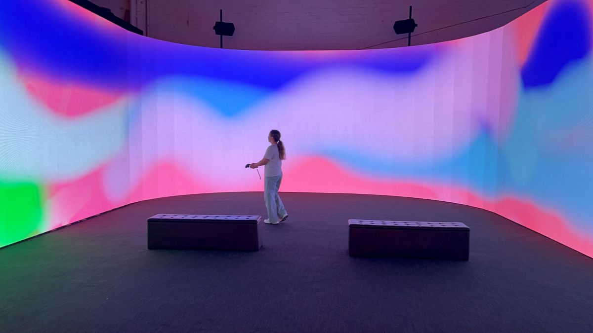 A woman stands before a large screen illuminated by vibrant, colorful lights, creating a dynamic visual backdrop.