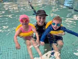 A woman and two children enjoying a sunny day together in a swimming pool, splashing and having fun.