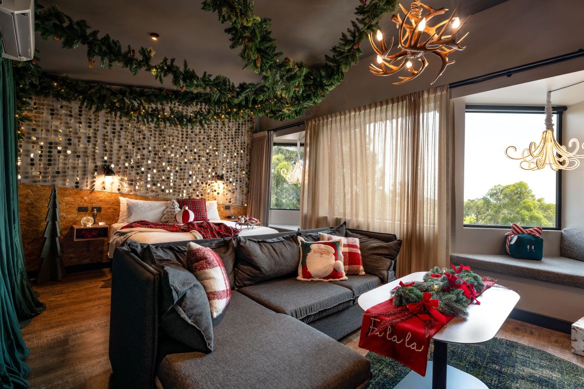 A festive bedroom scene showcasing a Christmas tree next to a plush couch, inviting warmth and holiday cheer.