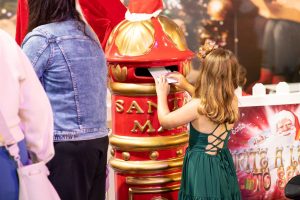 A young girl joyfully places a letter into a mailbox, showcasing her excitement and curiosity.