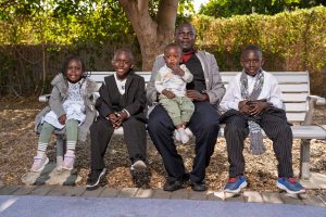 A man sits on a bench surrounded by four children, enjoying a moment of togetherness in a park setting.