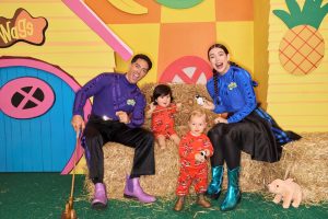 Two of The Wiggles smile with two children sitting on a stack of hay.