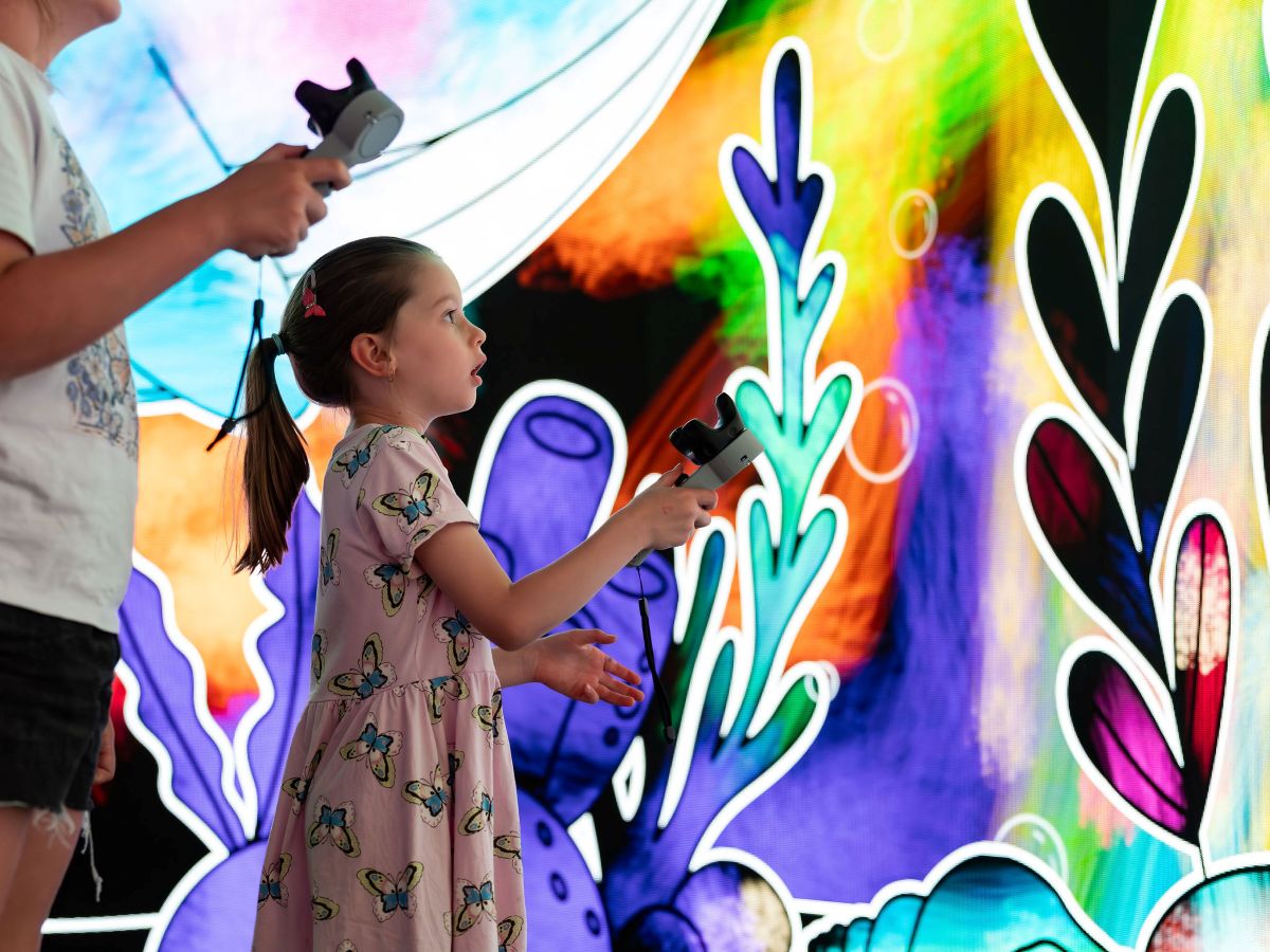  Two children joyfully playing a video game in front of a vibrant, colorful wall.