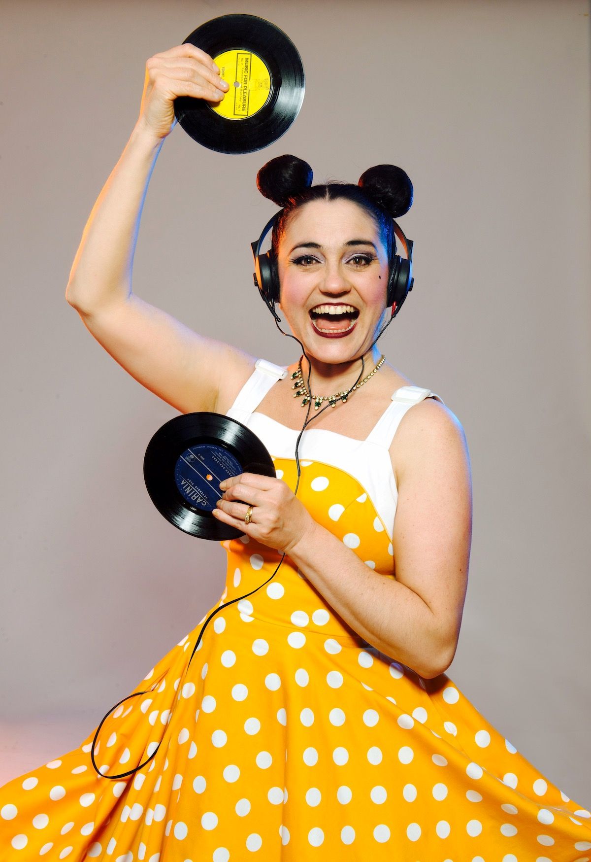 A woman in a polka dot dress joyfully holds two record players, showcasing her love for vintage music equipment.