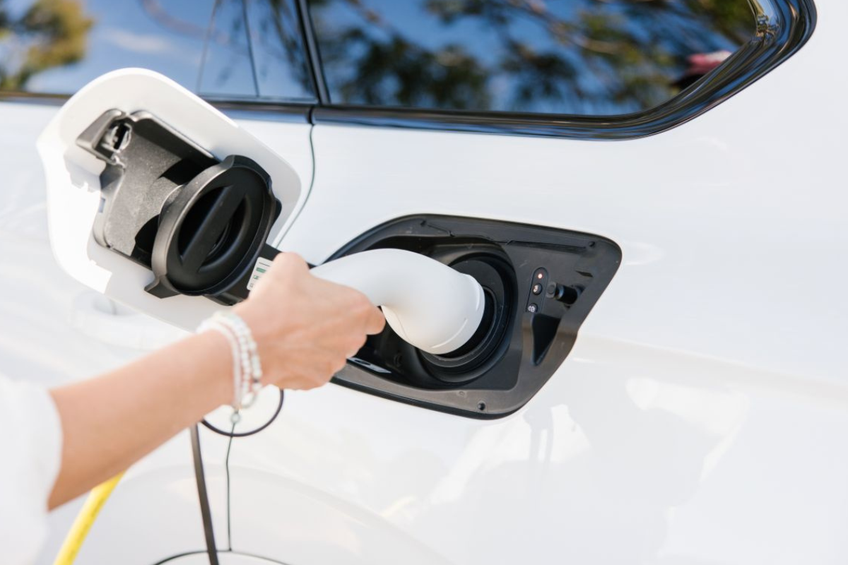 Close-up of a woman connecting a charging cable to an electric car at a charging station.