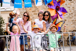 Mothers and children smiles together for a photo during a lively parade, surrounded by colorful floats and festive decorations.