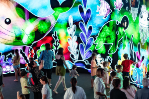 A group of people stands in front of a vibrant mural depicting an underwater scene filled with colorful marine life.