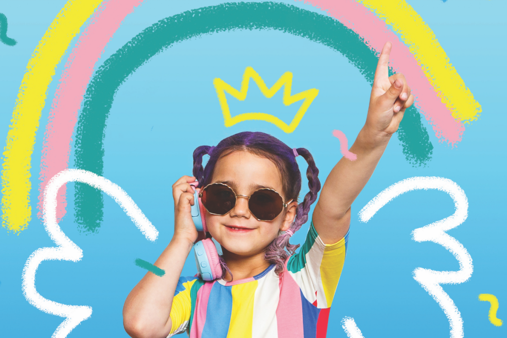 A girl with headphones and a colorful rainbow crown smiles, enjoying her music in a vibrant setting.