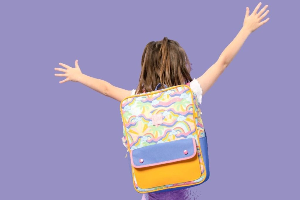 A girl stands with her arms outstretched, wearing a backpack, embracing the moment with joy and freedom.