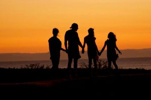 Silhouette of four people holding hands against a vibrant sunset backdrop, symbolizing unity and togetherness.