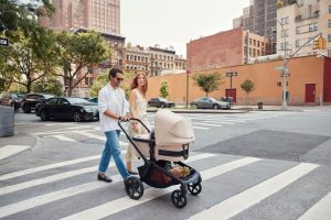 A man and woman stroll through the city, pushing a stroller as they enjoy their day together.