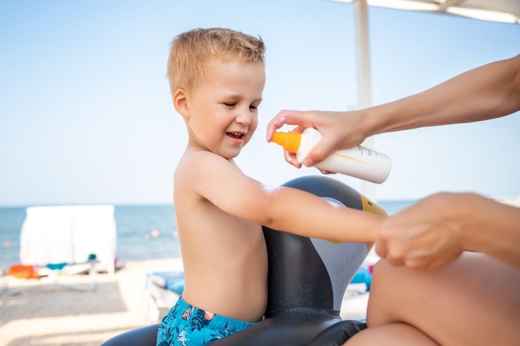 A child happily applies sunscreen to his arms on a sunny day, preparing for outdoor fun.