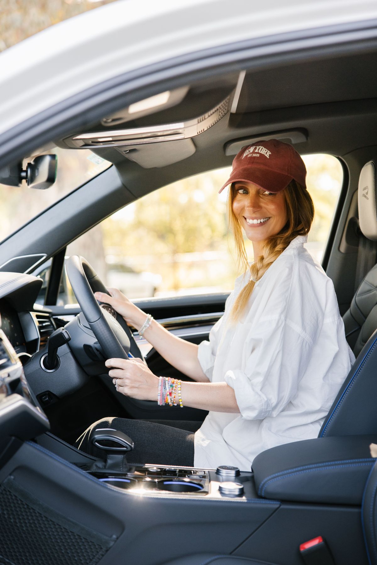 A woman in a hat is behind the wheel of a car, driving confidently.