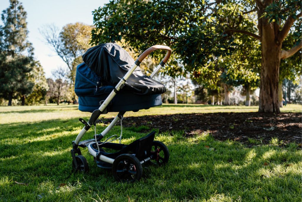 A stroller resting on green grass, surrounded by trees in the background, creating a serene outdoor scene.