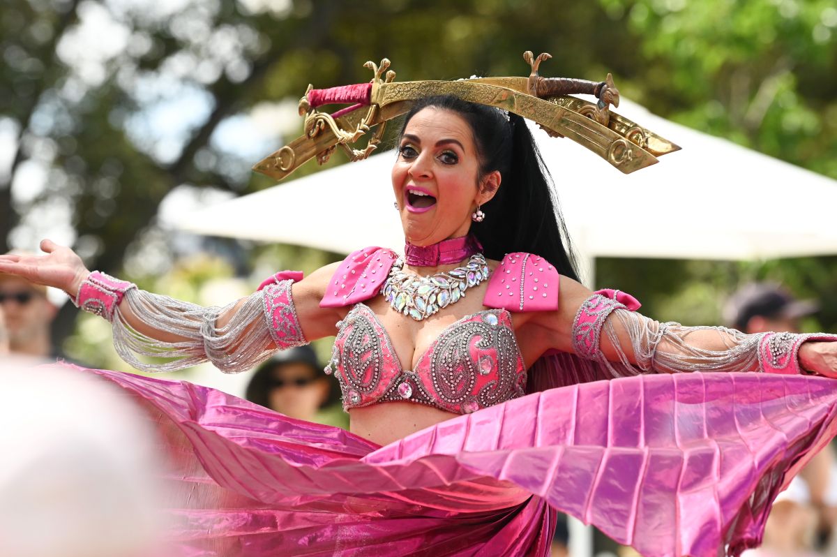 A woman in a vibrant pink costume dances joyfully under the bright sun, showcasing her graceful movements.