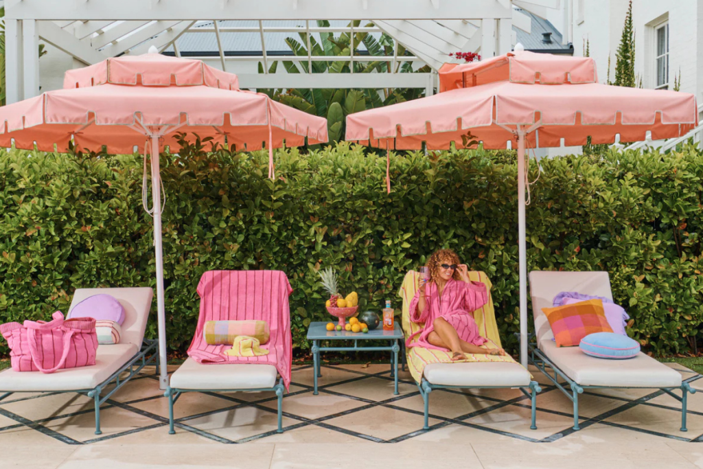 A woman relaxes on a lounge chair, surrounded by vibrant pink umbrellas on a sunny day.