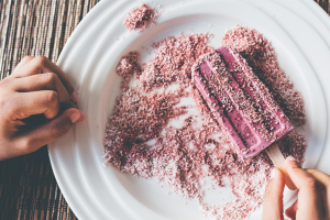 Close-up of a hand holding a pink ice cream bar, showcasing its vibrant color and creamy texture.