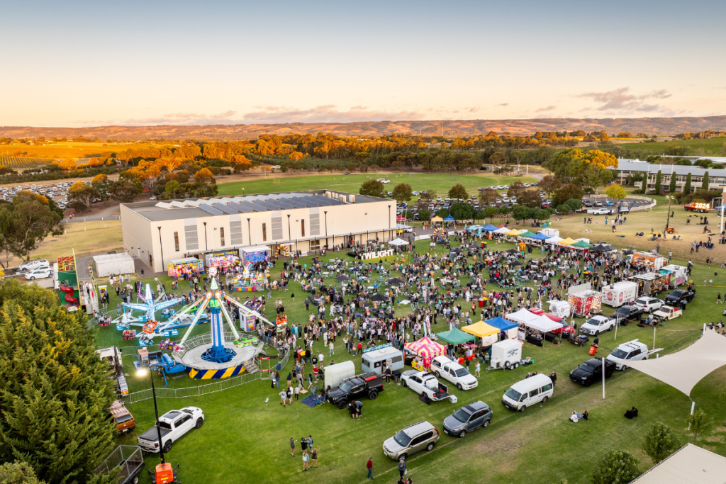 Aerial view of a bustling outdoor event featuring numerous cars and a crowd of people enjoying the festivities.