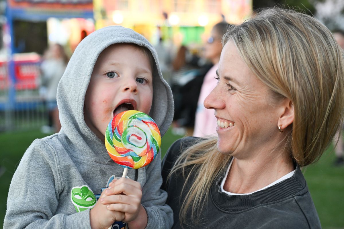  A woman lovingly holds a child who is enjoying a colorful lollipop, capturing a moment of joy and affection.