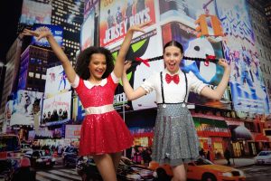 Two girls in red and white dresses pose together against a vibrant city skyline backdrop.