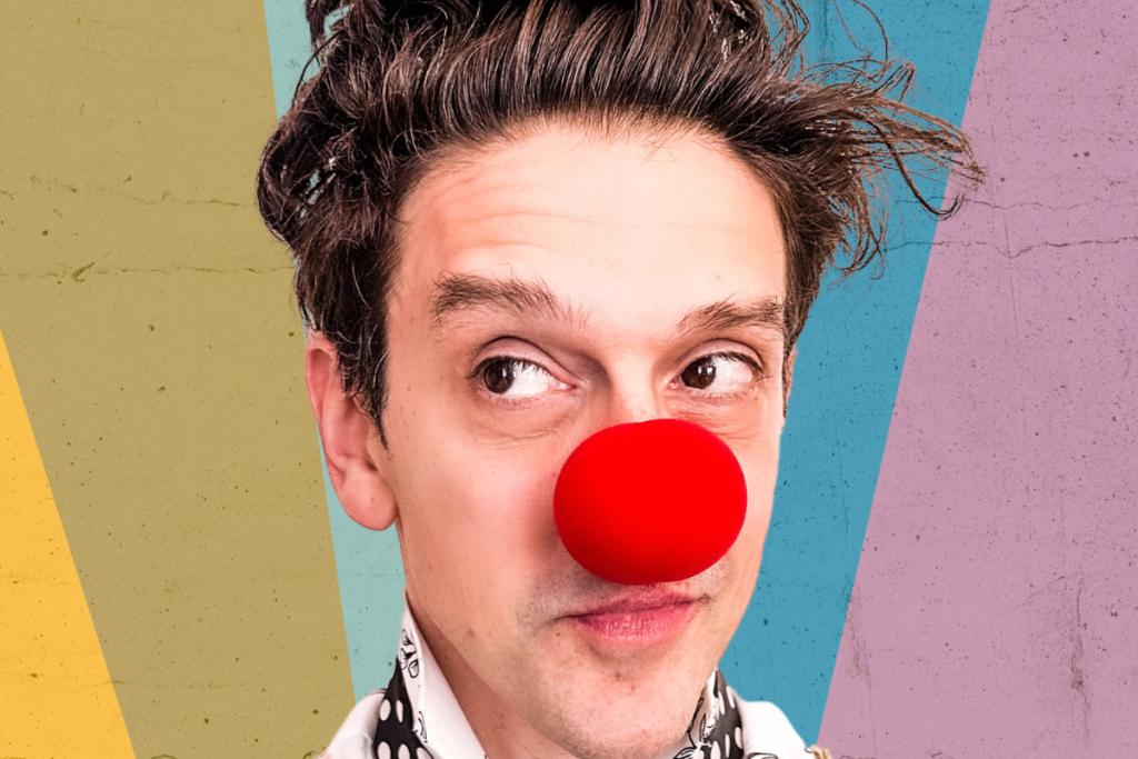 A man with a red nose wearing a classic clown nose, smiling playfully at the camera.