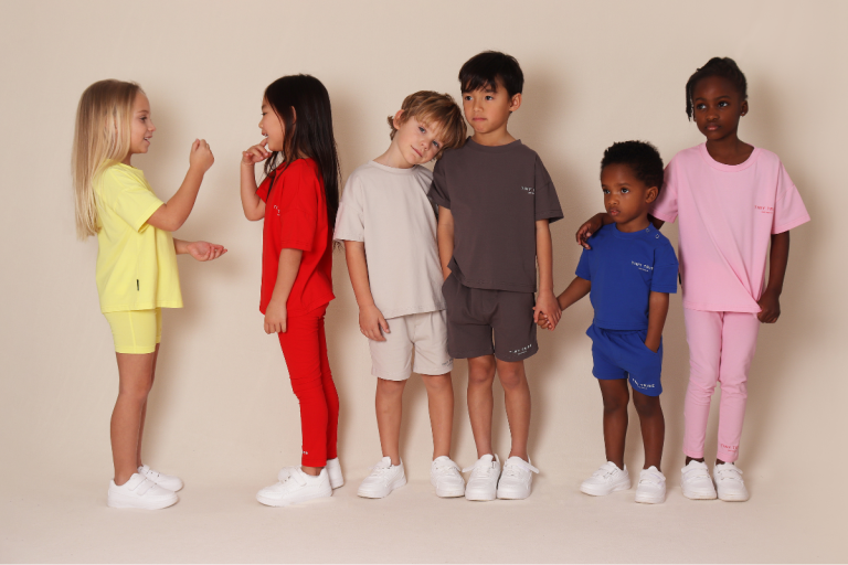 A diverse group of children dressed in various colorful outfits, smiling and enjoying their time together outdoors.