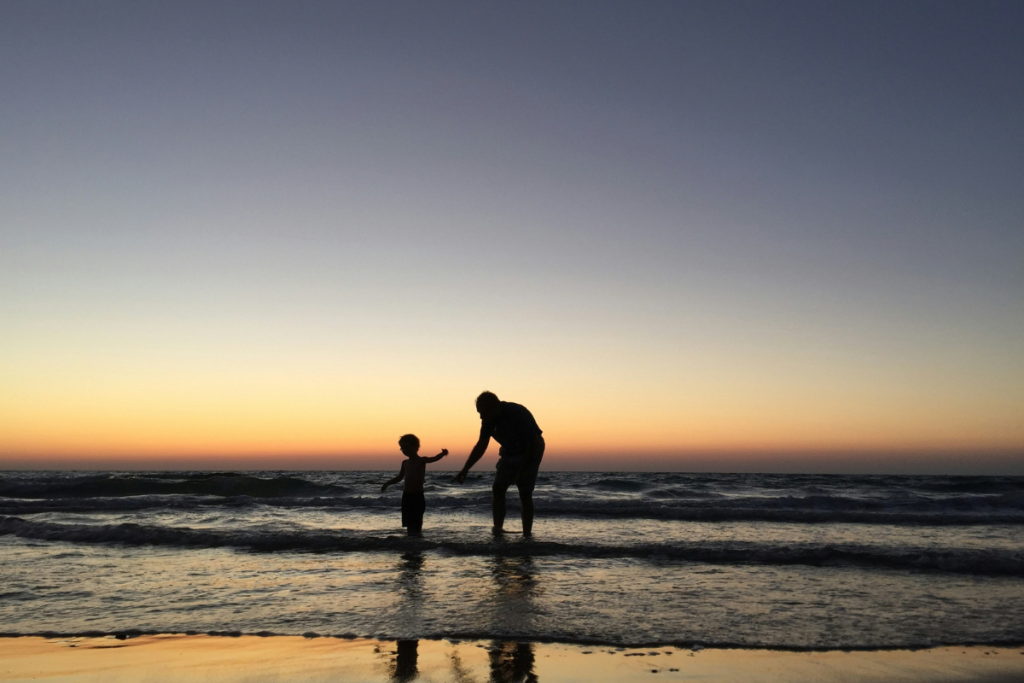 A father and son enjoying a sunset together on the beach, creating lasting memories in a serene setting.