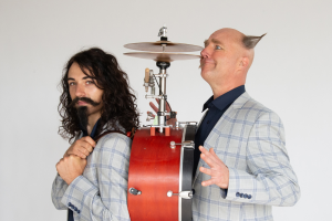 Two men with long hair play a drum set, showcasing their musical talent and passion for rhythm.