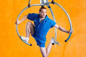 A man in blue shorts performs a trick on a hoop, showcasing his skills and balance in a dynamic pose.