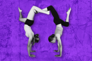 Two women performing handstands against a vibrant purple background, showcasing strength and balance.