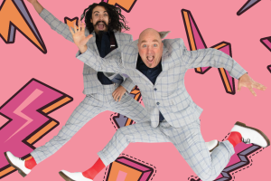 Two men in suits joyfully jumping against a vibrant pink background, showcasing energy and enthusiasm.