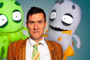 A man in a suit and tie stands beside three colorful cartoon characters, smiling and posing for the camera.