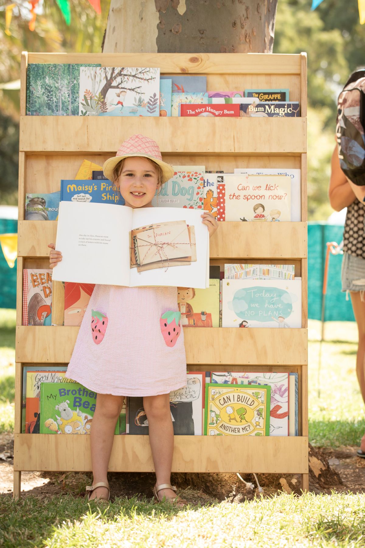 A little girl stands in front of a bookcase, joyfully holding a book in her hands.