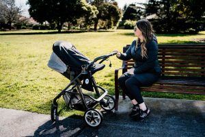 A woman seated on a park bench beside a baby stroller, enjoying a peaceful moment in a serene outdoor setting.