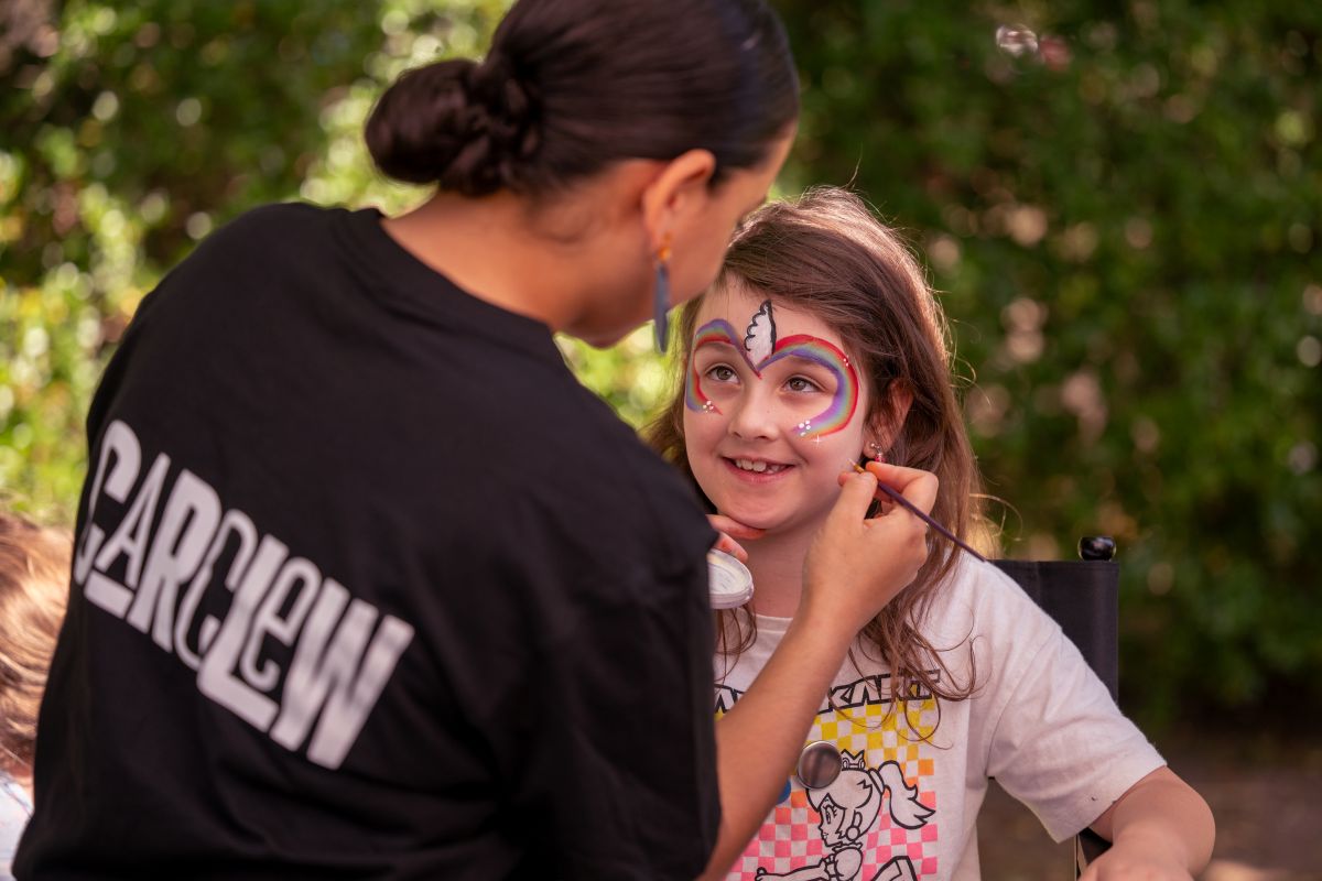 A woman carefully paints a young girl's face with colorful designs, creating a joyful and artistic moment.