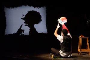 A man performs on stage, skillfully holding a puppet, captivating the audience with his lively act.