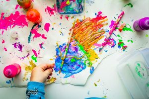 A child's hand grips a paintbrush, creating colorful strokes on a blank white canvas.