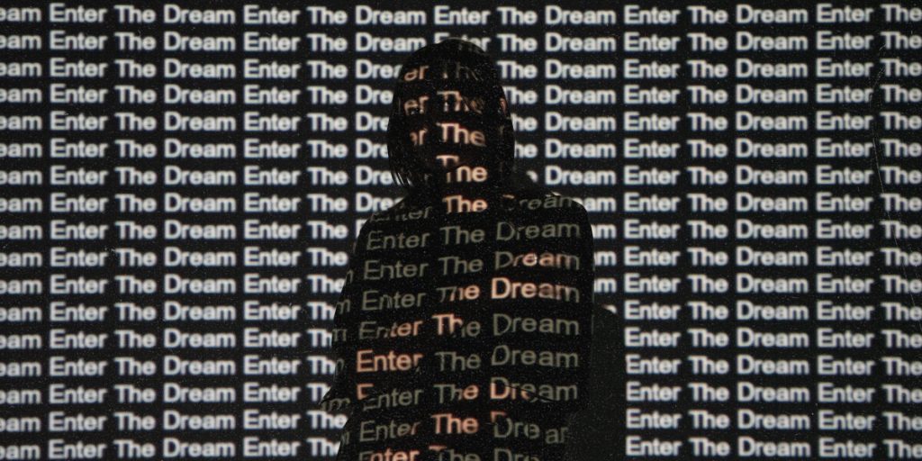 A person stands silhouetted against a wall featuring the phrase "enter the dream."